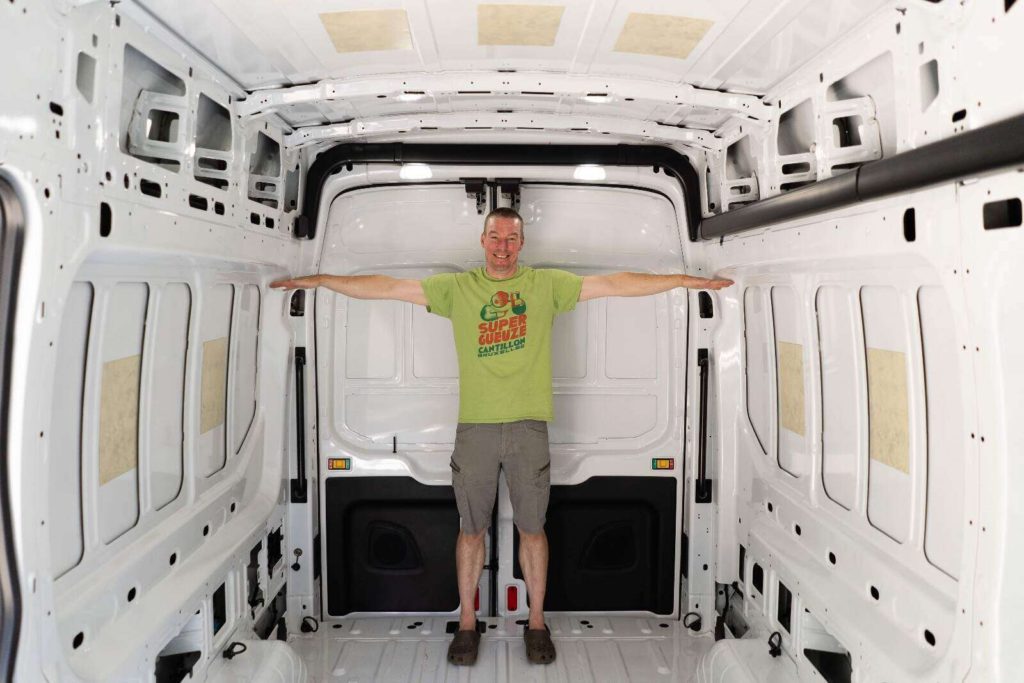 Standing man showing arms length width comparison of Ford Transit cargo van interior for camper van conversion.